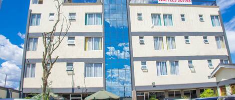 A multi-story hotel with a sign reading "The Waffles Suites" and a large glass window reflecting the sky.