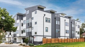 Un edificio residencial de varios pisos con un diseño moderno, que cuenta con balcones, una valla de madera y un cielo despejado.