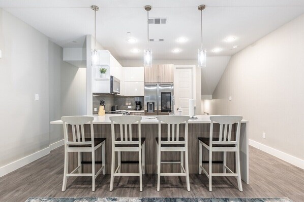 Una cocina moderna con armarios blancos, una isla central con taburetes y luminarias colgantes.