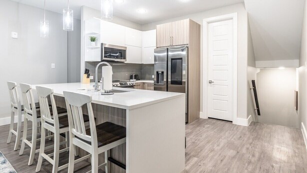 Una cocina moderna con una isla central, armarios blancos, electrodomésticos de acero inoxidable e iluminación colgante.