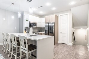 A modern kitchen with a central island, white cabinetry, stainless steel appliances, and pendant lighting. - Magnolia District Modernism- Sleek 2-Bed Escape (Fort Worth)