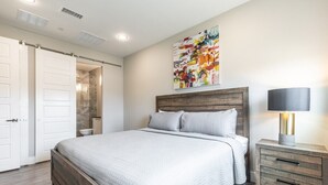 Un dormitorio con cama, mesita de noche, un cuadro y la puerta del baño.