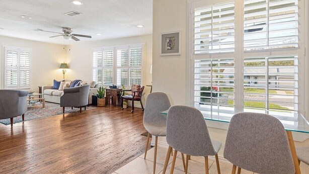 A spacious living room with hardwood flooring, a ceiling fan, and large windows with blinds. - Mary’s Mid-Century Modern House- 3-Bed Haven (Fort Worth)
