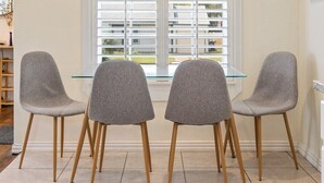A dining area with three grey chairs and a glass table, a window with blinds, and a framed picture on the wall. - Mary’s Mid-Century Modern House- 3-Bed Haven (Fort Worth)