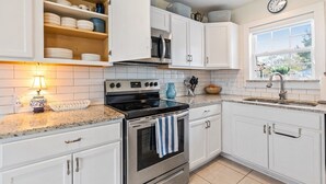 A kitchen with white cabinets, a stainless steel stove, a microwave, and a sink. - Mary’s Mid-Century Modern House- 3-Bed Haven (Fort Worth)