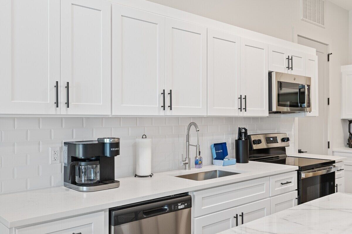 A modern kitchen with white cabinets, a stainless steel microwave, a coffee maker, and a dishwasher.