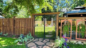 A garden with a wooden fence, a metal gate, and a stone pathway leading to a gazebo. - Your Downtown Oasis 14-foot ceilings, luxury living. Relaxing outdoor spaces (Elora)