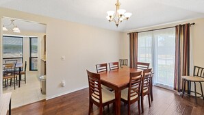 A dining area with a wooden table and chairs, a chandelier, and large windows with curtains. - Cozy Nest-3-Bedroom Charm In Plano (Plano)