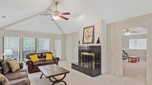 A spacious living room with a fireplace, leather sofas, and a ceiling fan. - Cozy Nest-3-Bedroom Charm In Plano (Plano)