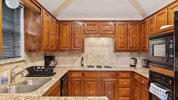 A kitchen with wooden cabinets, granite countertops, a stainless steel sink, a stove, and an oven. - Cozy Nest-3-Bedroom Charm In Plano (Plano)