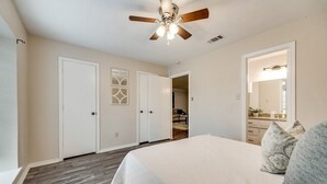 A bedroom with a bed, a ceiling fan, a wardrobe, and a bathroom visible through an open door.