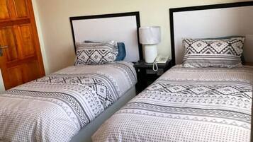 A room with two beds, each with patterned bedding and a nightstand with a lamp.