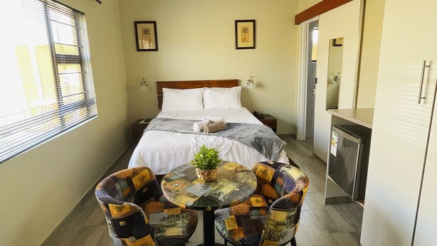 Une chambre d’hôtel avec un lit, une petite table avec des chaises, une plante en pot et une kitchenette.