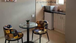 Une cuisine compacte équipée d’un four à micro-ondes, d’un petit réfrigérateur et d’une fenêtre. On y trouve également un coin repas avec une table en verre et deux chaises.