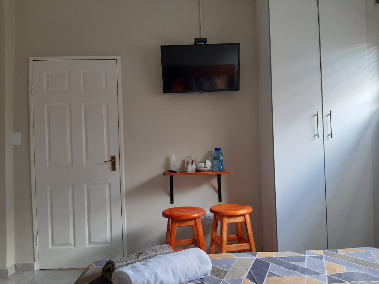 A bedroom with a bed, a TV mounted on the wall, a small shelf with toiletries, and a wardrobe.