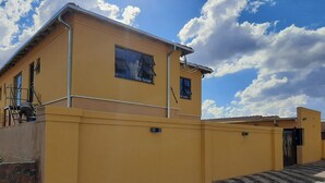 Un bâtiment jaune avec un chemin pavé de briques menant à une entrée fermée par un portail.
