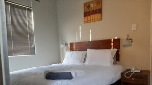 Un lit bien fait, avec du linge de lit blanc, une tête de lit en bois et une table de chevet sur laquelle se trouve un téléphone.