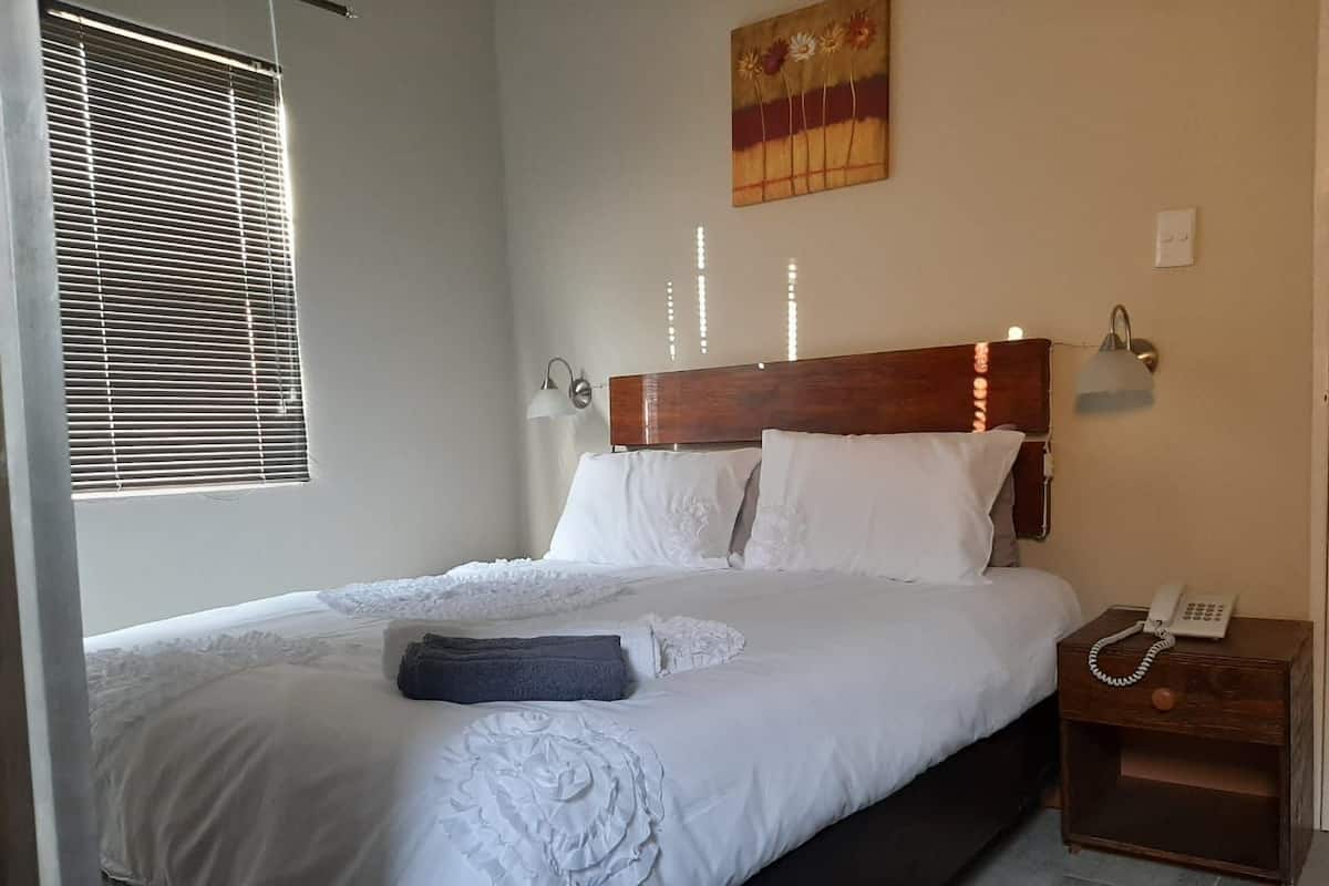 Una cama bien hecha con sábanas blancas, un cabecero de madera y una mesita de noche con un teléfono.