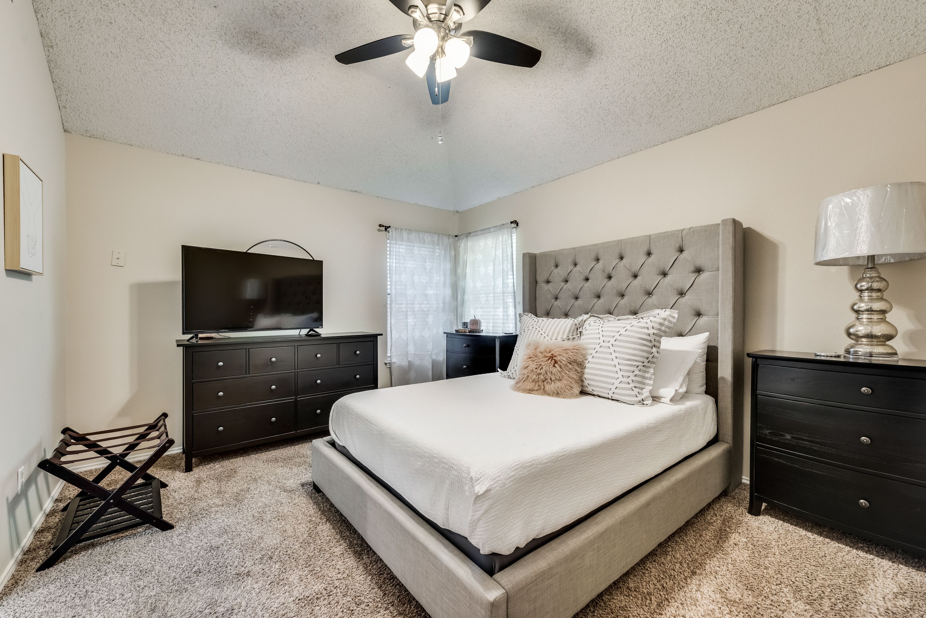 A bedroom with a large bed, a ceiling fan, a TV, and a dresser.
