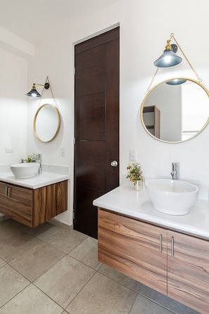 A modern bathroom with two sinks, wooden cabinets, and a dark door.