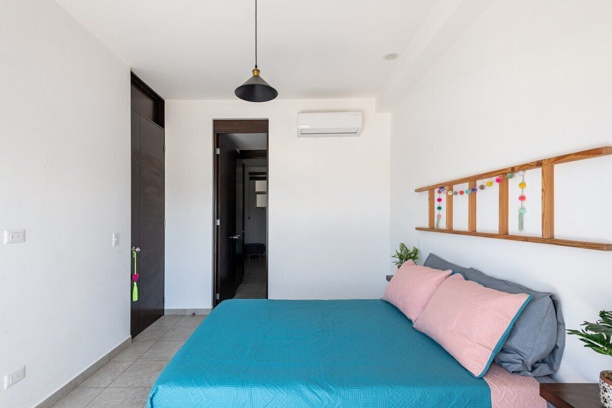 Ein Schlafzimmer mit einem Bett, einer Hängelampe, einem Regal mit Dekoration und einer Klimaanlage.