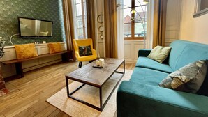 A living room with a teal sofa, a yellow armchair, a wooden coffee table, a bench, and a television mounted on the wall. - Apartment in Verdun, "La Scène du 66" (Verdun)