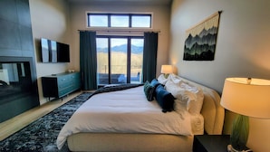Habitación de hotel moderna con una cama grande, televisión de pantalla plana, escritorio y vistas a las montañas a través de las ventanas.