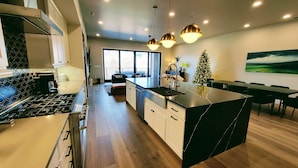 Una cocina moderna con una isla central, iluminación colgante y un comedor con vistas.