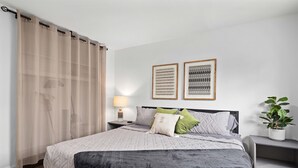 Ein ordentlich bezogenes Bett mit Steppdecke, eine Nachttischlampe und ein Nachttisch mit einer Pflanze.