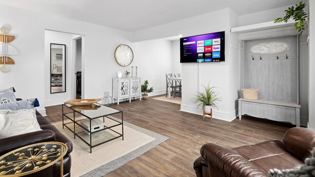 Ein modernes Wohnzimmer mit Flachbildfernseher, Ledersofas, einem Essbereich und einer weißen Wand mit einer Uhr.