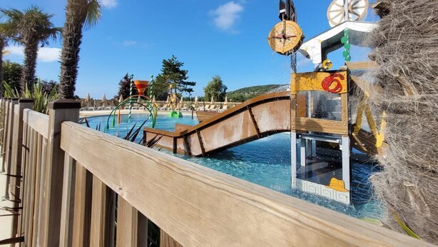 Une clôture en bois entoure une zone de piscine, qui comprend un pont et un élément décoratif aquatique.