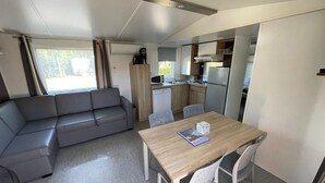 Un espace de vie compact comprenant un canapé, une table à manger, des chaises, un coin cuisine et une fenêtre.