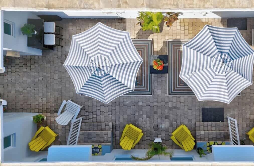 A rooftop terrace with two large striped umbrellas, a pool, and yellow lounge chairs.