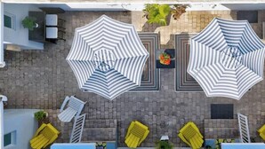 Terraza en la azotea con dos grandes sombrillas a rayas, una piscina y sillones de descanso amarillos.