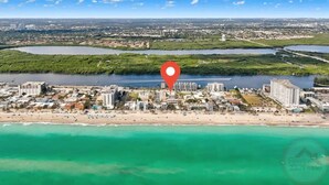Vista aérea de una ciudad costera con una playa destacada, un río y un marcador rojo que indica una ubicación.
