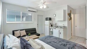 Un dormitorio moderno con cama, un escritorio pequeño, un sofá y una kitchenette.