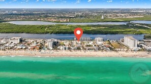 Vue aérienne d’une ville côtière avec un hôtel en bord de mer, entouré d’étendues d’eau et de verdure.
