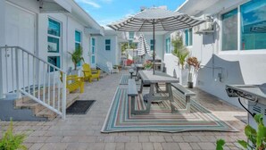 A patio area with a table and chairs, a striped umbrella, and a staircase leading to an upper level. - Sunny Serenity: Hollywood Studio Getaway (Hollywood)