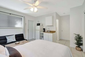 Un dormitorio con una cama grande, ventilador de techo, kitchenette y una pequeña planta en maceta.