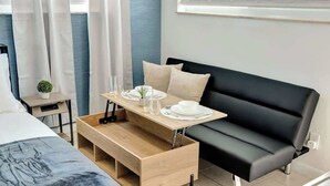 Ein modernes Schlafzimmer mit einem Bett, einer Holzbank, einem schwarzen Sofa und einem kleinen Tisch mit weißem Teller und Glas.