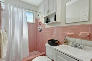 Un baño con ducha, inodoro, lavabo y repisas con artículos de aseo.