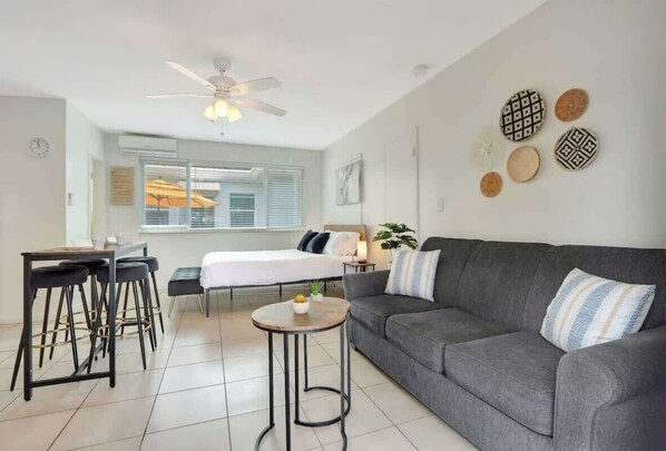 A modern living room with a grey sofa, a round coffee table, and a dining area with a table and chairs.