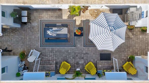 An aerial view of a rooftop patio with a pool, sun loungers, and umbrellas.