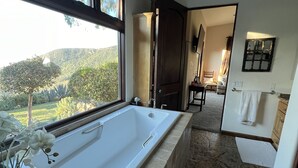 A modern bathroom with a large bathtub, a view of a garden, and a wooden door leading to another room. - Guesthouse in very private location in Malibu with ocean views!
 (Malibu)