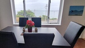 Un comedor con mesa y sillas, una ventana con vista al mar y líneas eléctricas, y un cuadro en la pared.