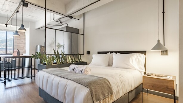 Ein modernes Schlafzimmer mit einem großen Bett, einem Nachttisch und Blick ins Freie.