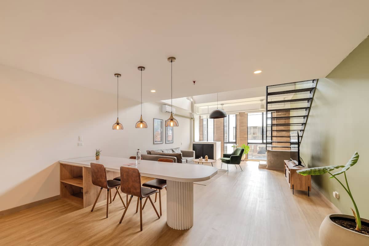 Een moderne keuken met een centraal eiland, houten vloeren, hanglampen en een trap met een metalen leuning.