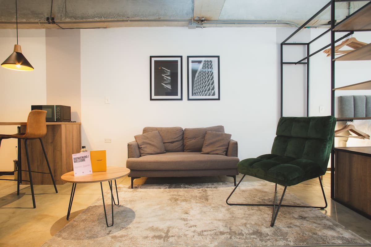 Een moderne woonkamer met een bank, een groene fauteuil, een salontafel en een hanglamp. Twee ingekaderde foto's hangen aan de muur.