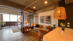 Ein modernes Wohnzimmer mit einem großen Glasfenster zum Balkon, Holzboden, einem runden Esstisch und einer Pendelleuchte.