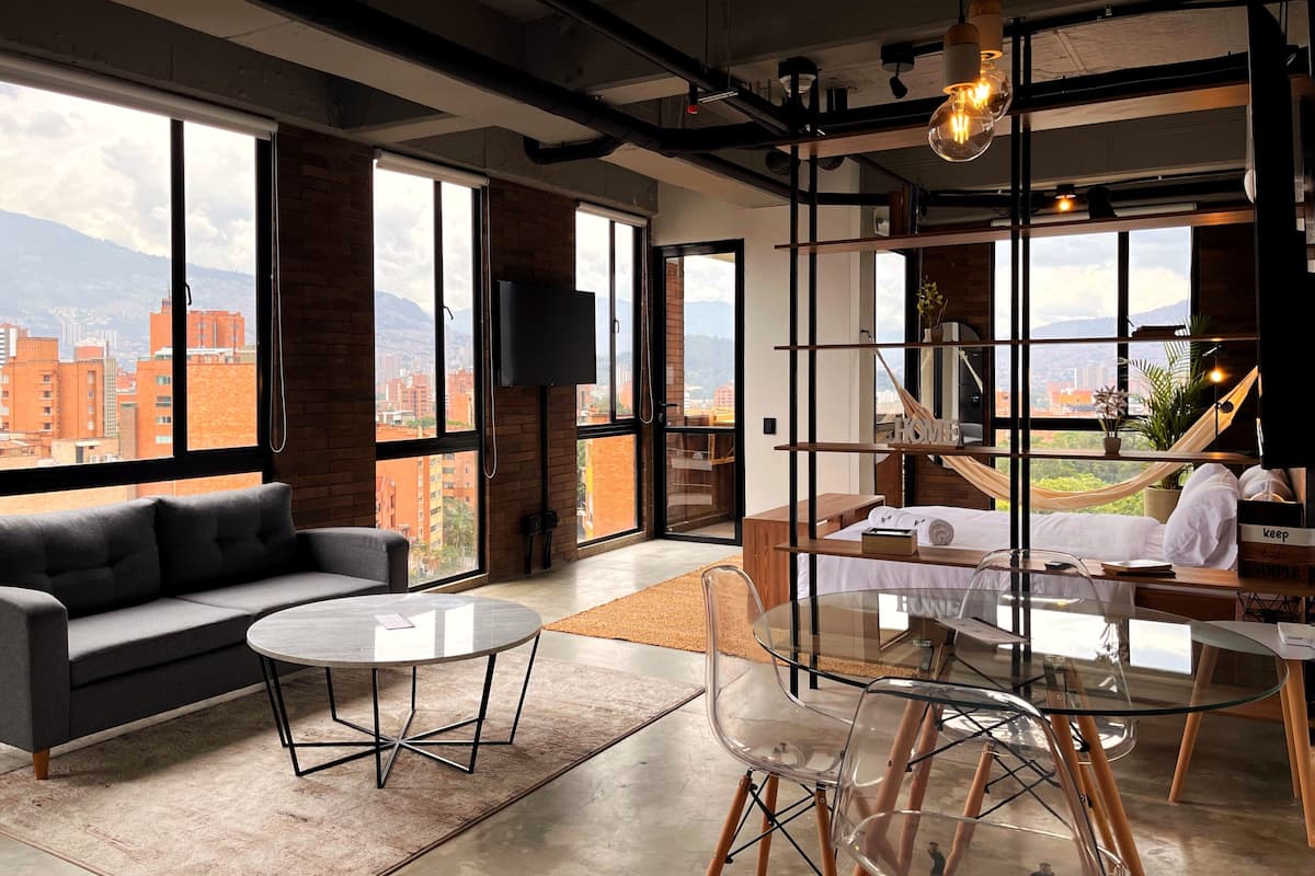Een moderne hotelkamer met grote ramen, een bank, een ronde tafel en een glazen eethoek.